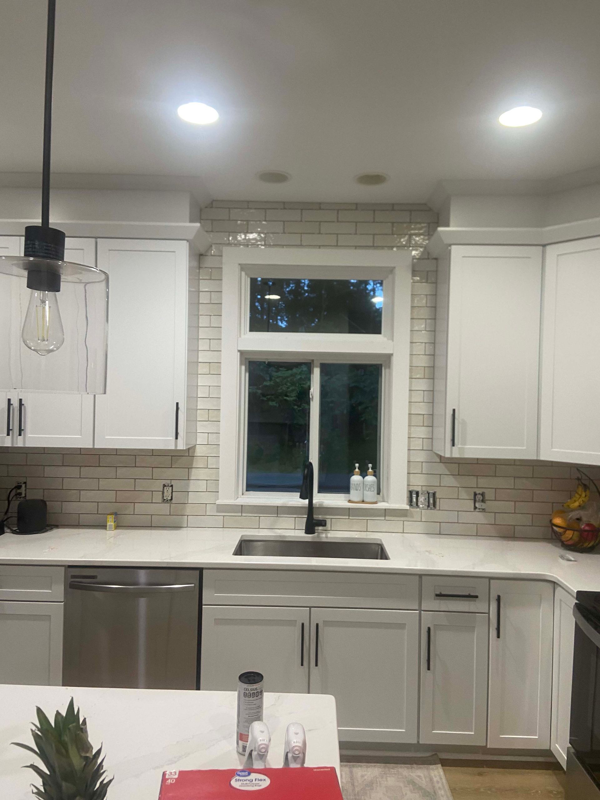 Bright white kitchen with island, sink under window, and pendant light over counter