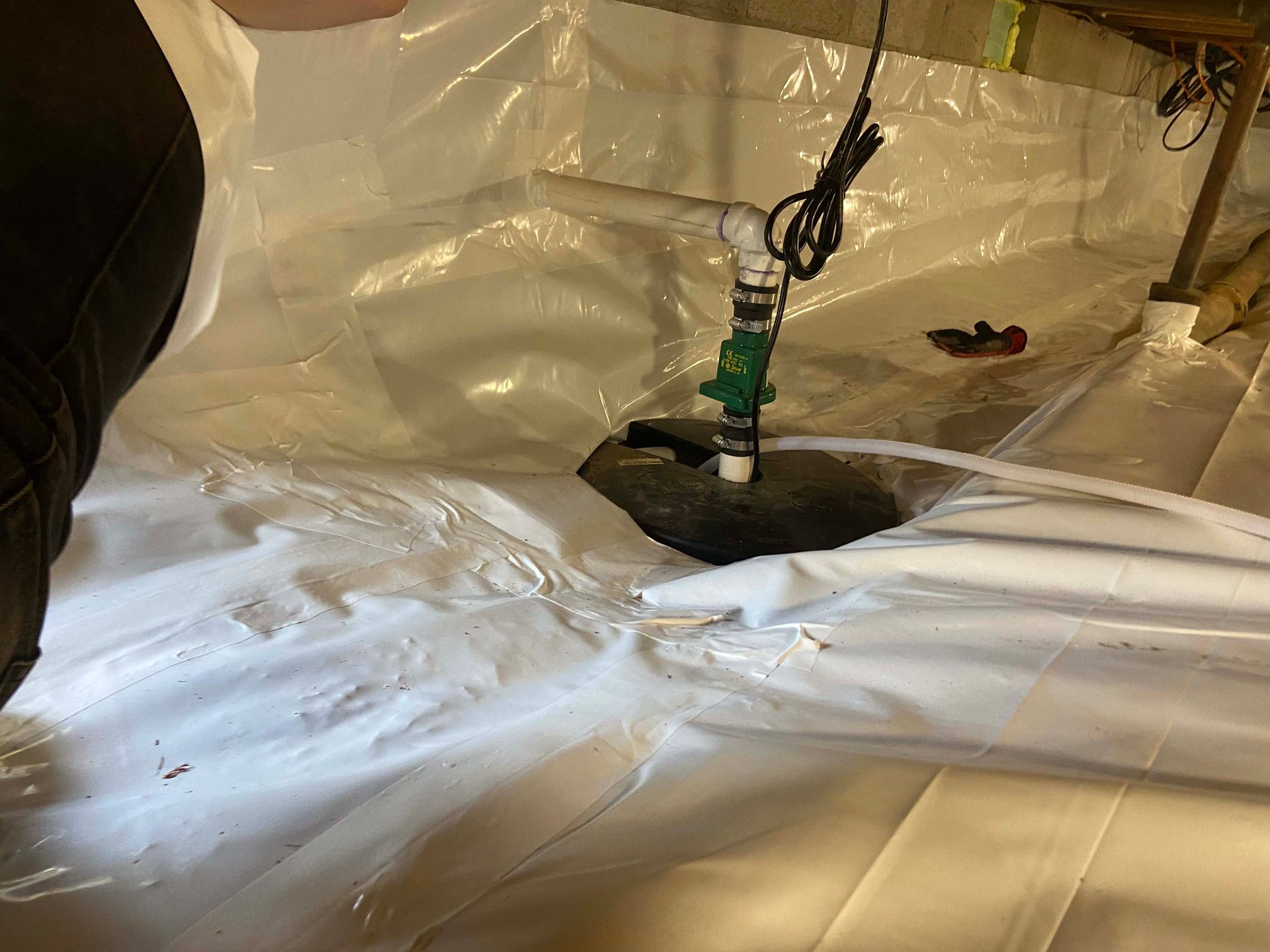 White plastic sheeting around a dark circular hole with a green pipe or tool hanging above it