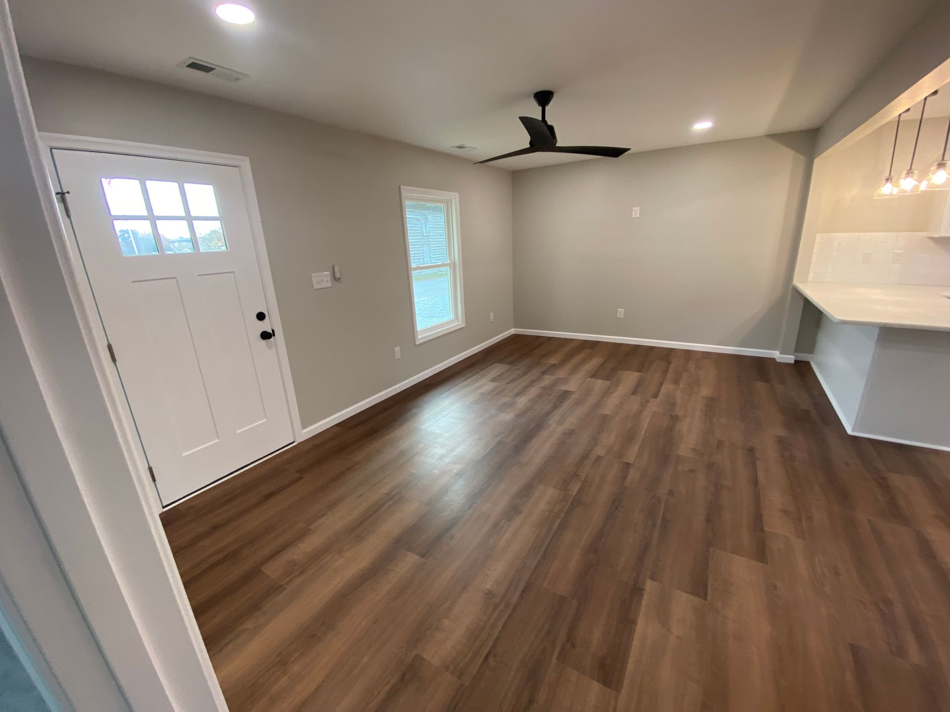 Empty living room with wood floors, gray walls, white door, and ceiling fan.
