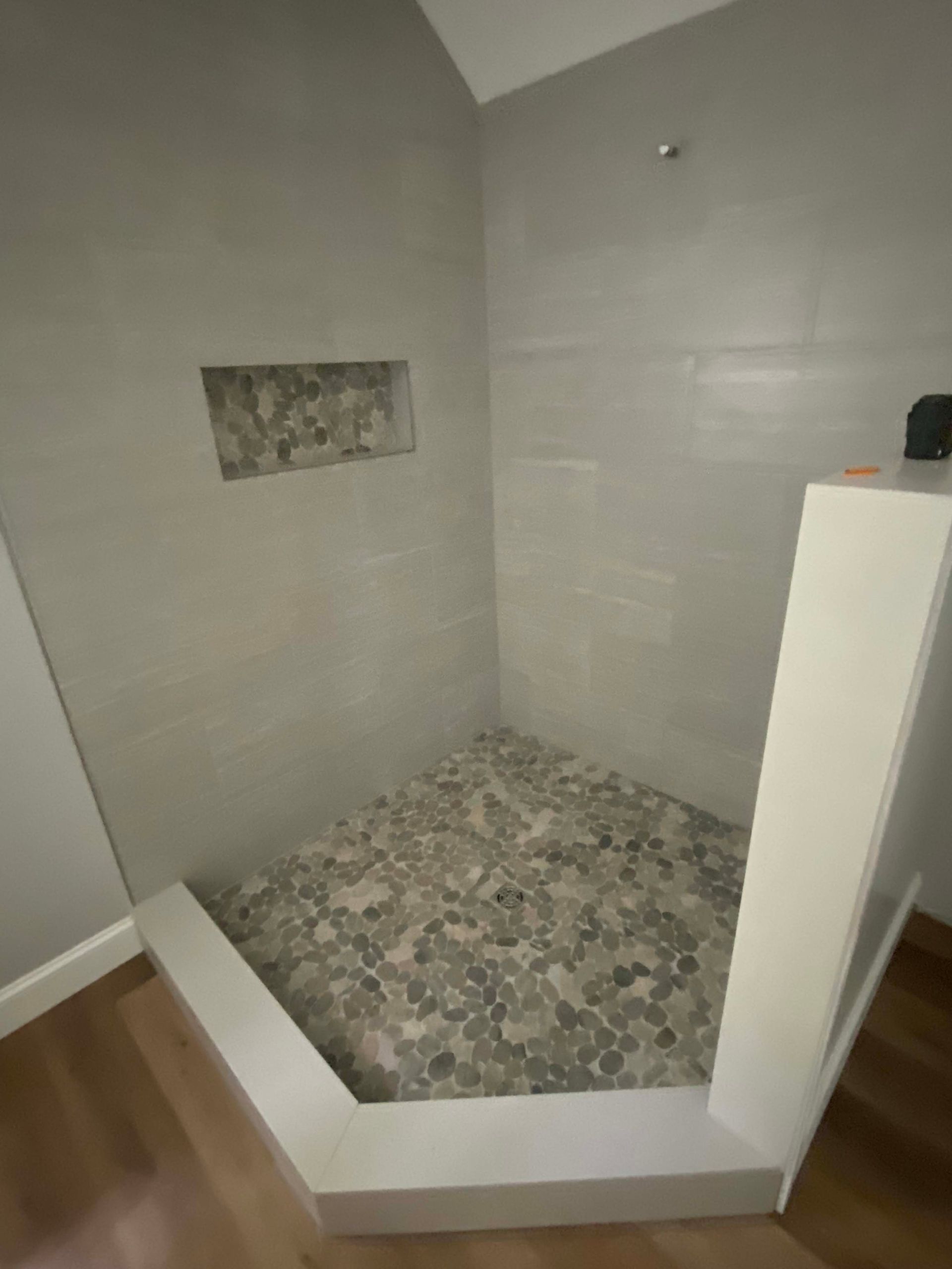 Walk-in shower with white tiled walls, mosaic floor, and a recessed wall niche.