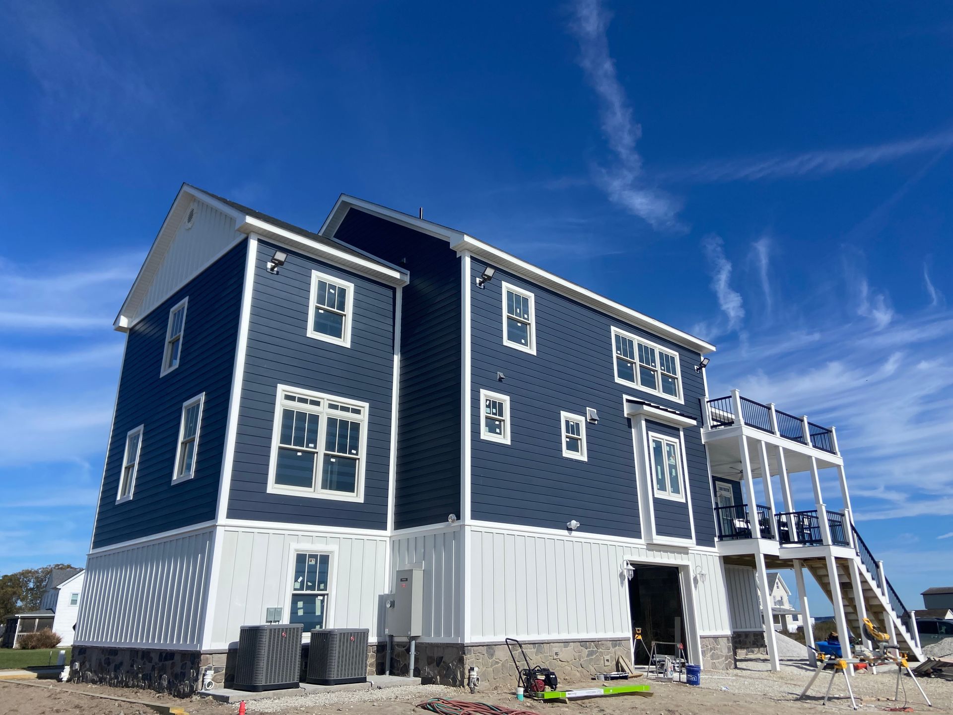 Blue house under construction with white trim and a deck, against a clear blue sky