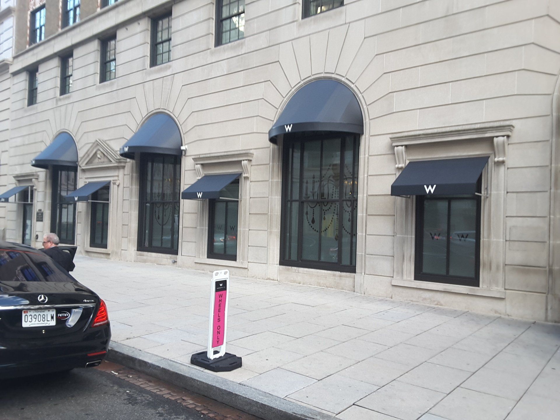 A car is parked in front of a building with awnings on the windows.