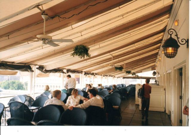A group of people sitting at tables under a ceiling fan.