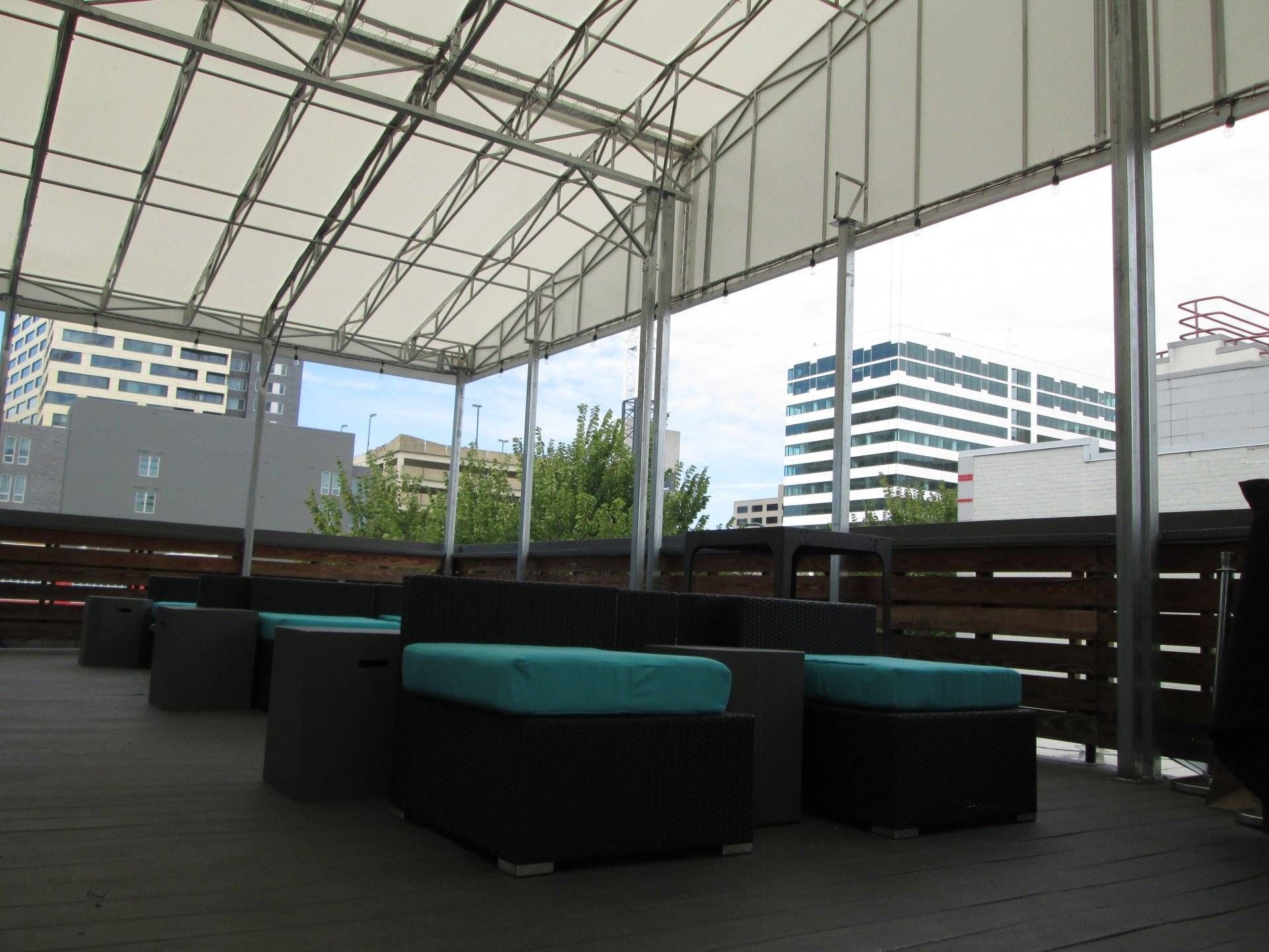 A rooftop deck with a couch and ottomans under a canopy.