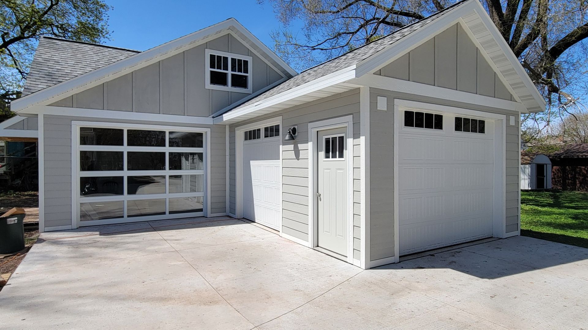 White detached garage with a glass-paneled door beside a light gray house driveway.