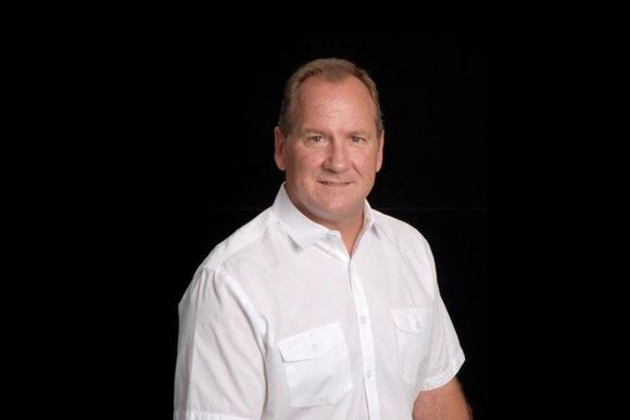 A man in a white shirt is standing in front of a black background.