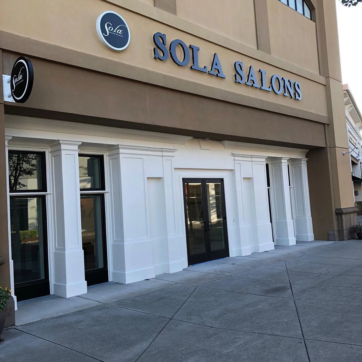 Sola Salons storefront with white columns, black doors, and sign. Beige building.