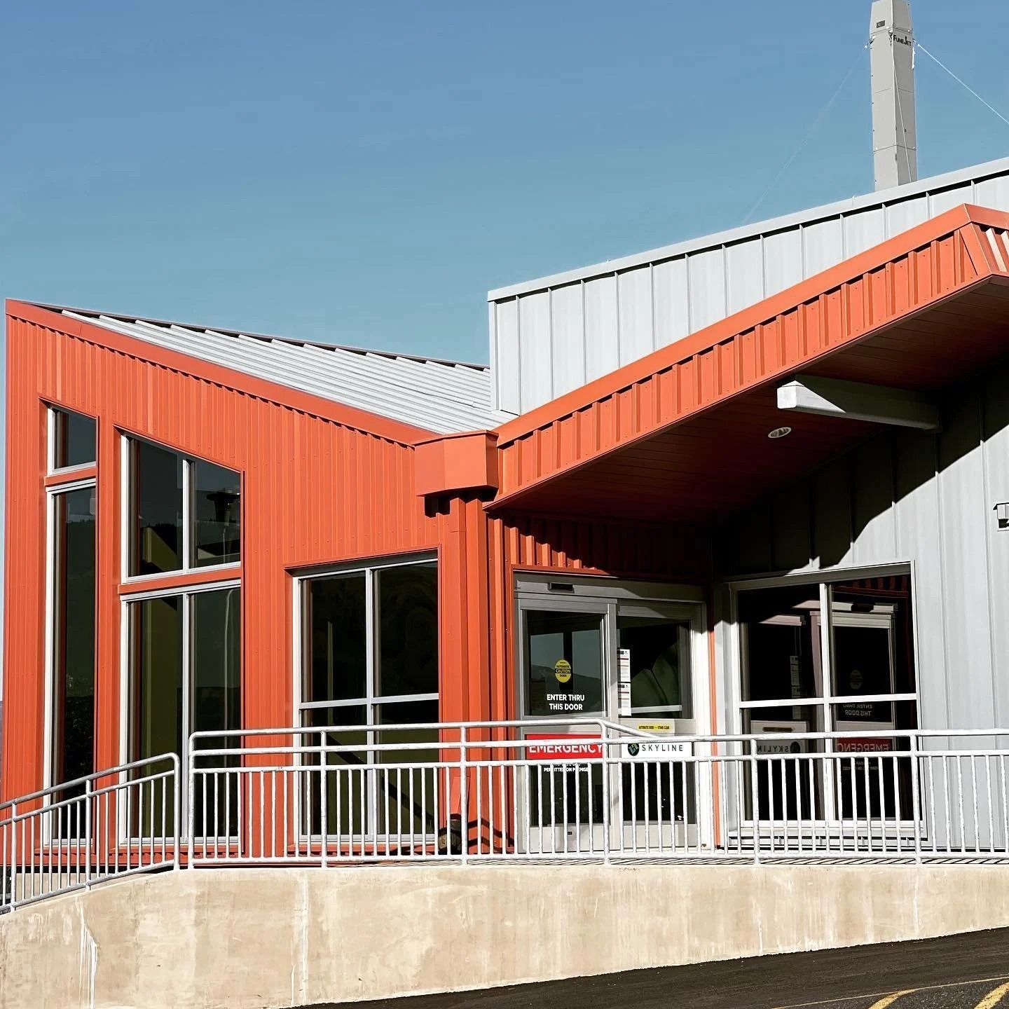 Orange and grey building with large windows and a ramp entrance.