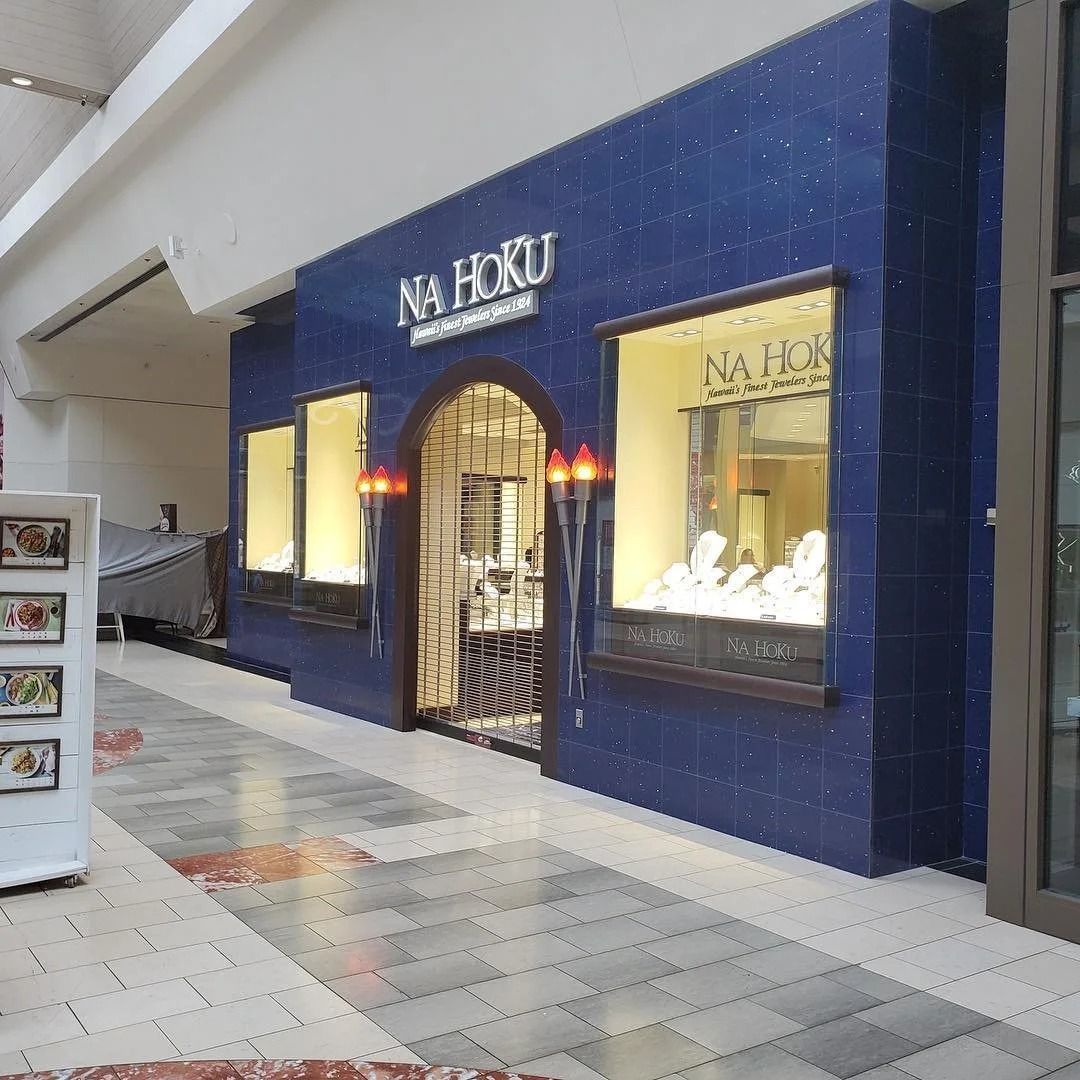 A blue jewelry store, NA HORU, has lit display windows in a mall.
