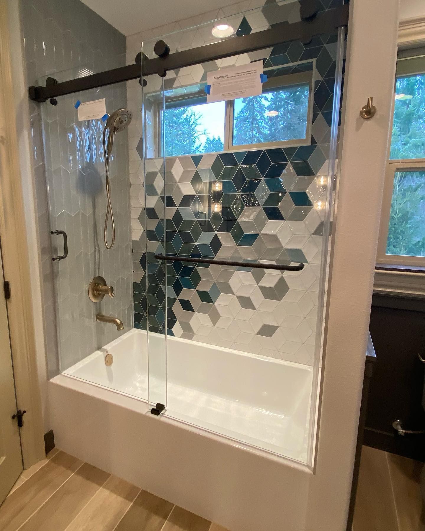 Bathroom with white bathtub, glass shower door, and geometric blue and gray tile.