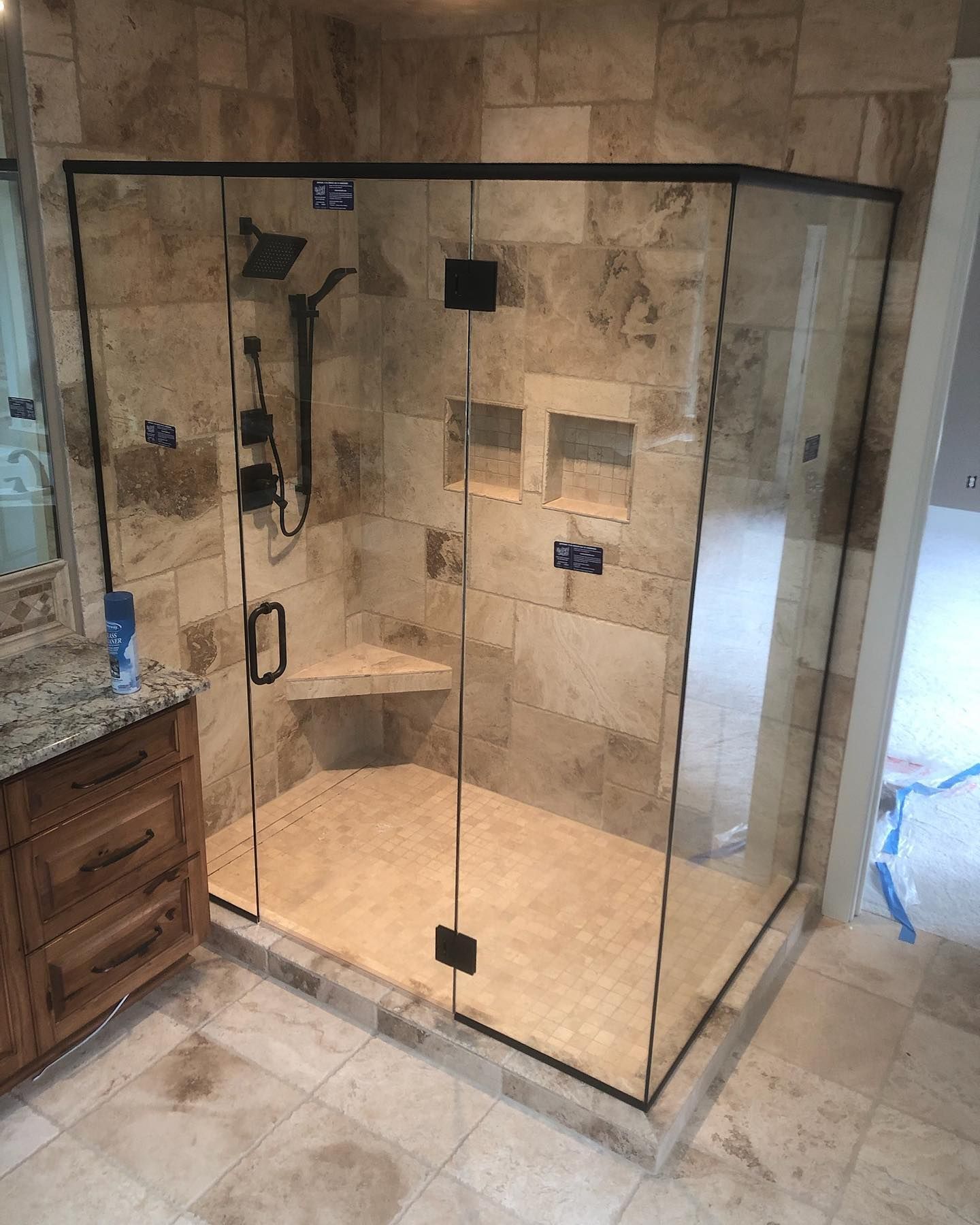 Shower with glass enclosure, beige tiled walls, black fixtures, and a granite vanity.