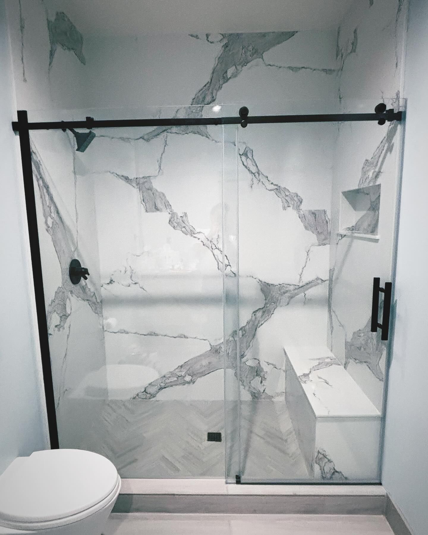 Modern bathroom with marble-look shower, sliding glass door, black hardware, built-in bench, and a toilet.