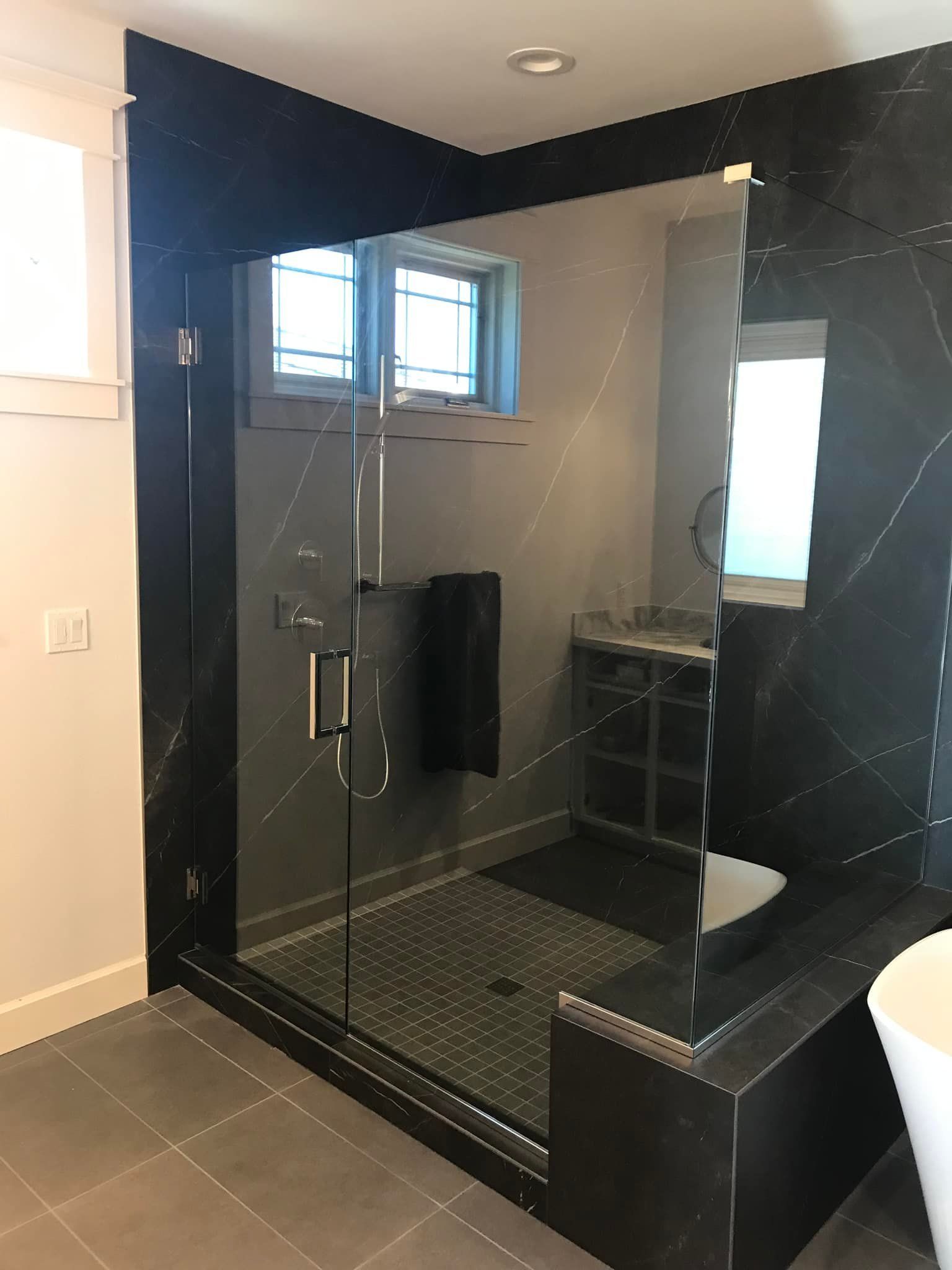 Modern bathroom with black tiled shower, glass door, and gray floor.