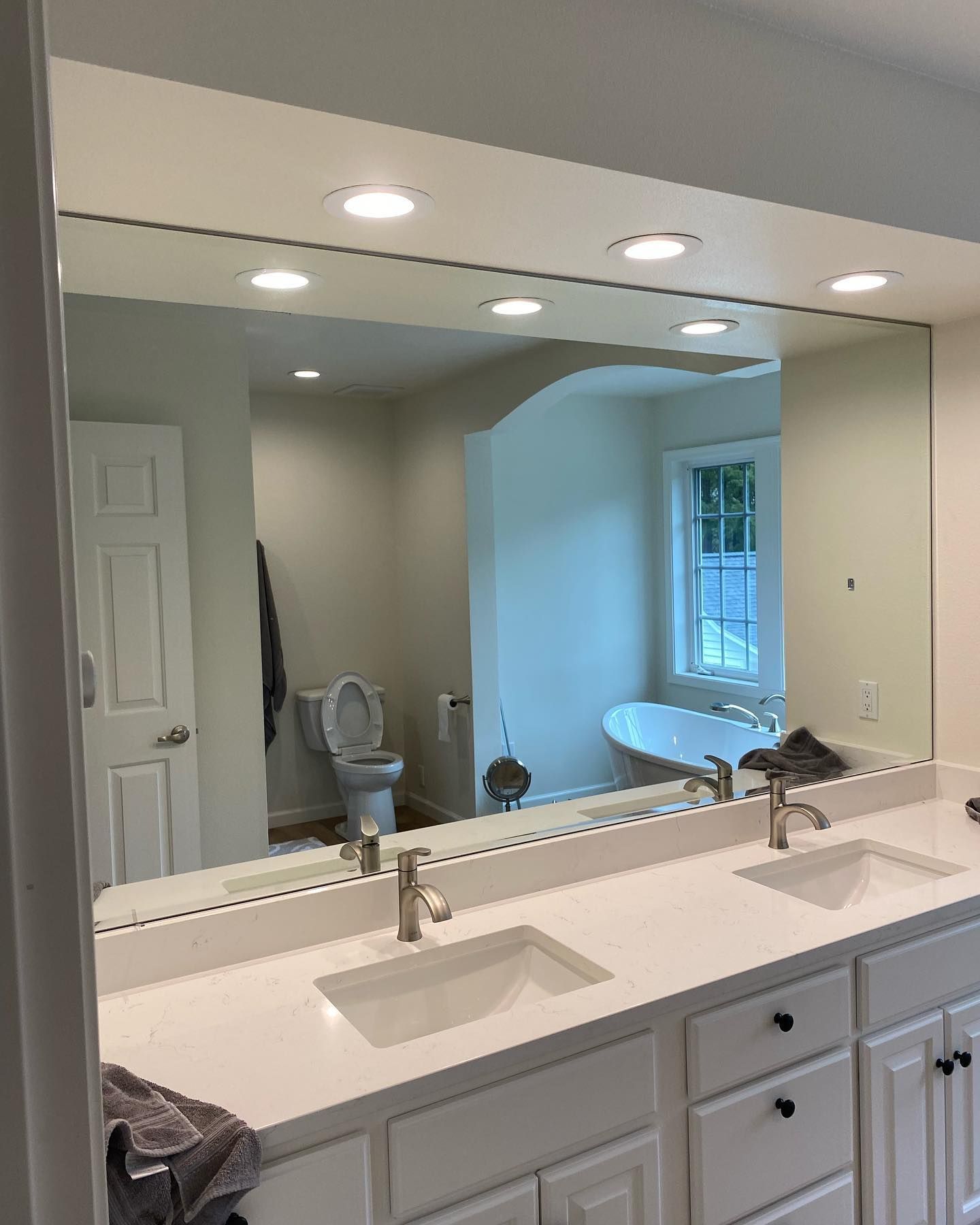 Bathroom with white vanity, large mirror, two sinks, toilet, and bathtub.