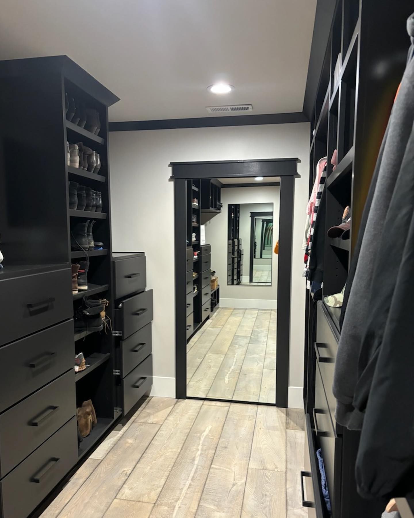 Walk-in closet with dark cabinets, light wood floor, and doorway to another closet with a full-length mirror.