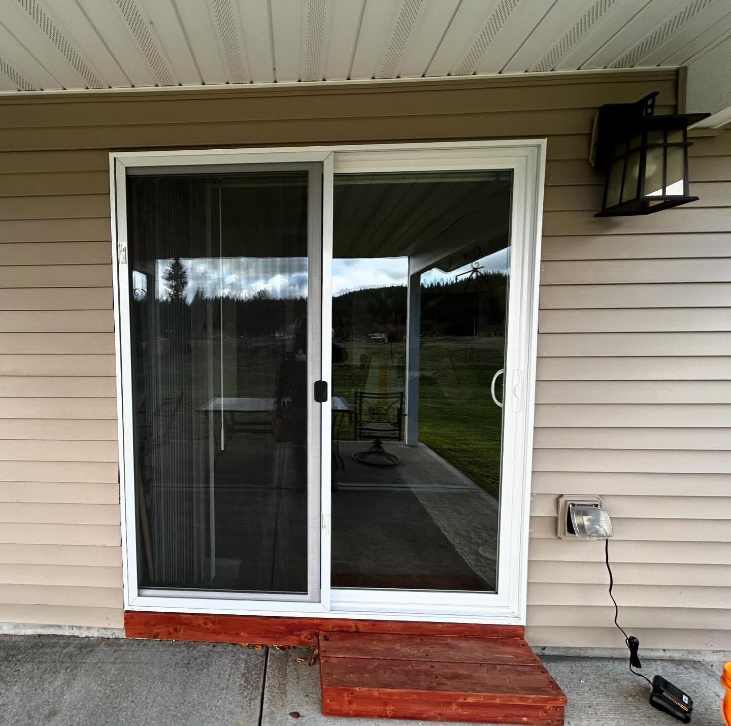 White sliding glass door with screen, red step, and outdoor light on beige siding.