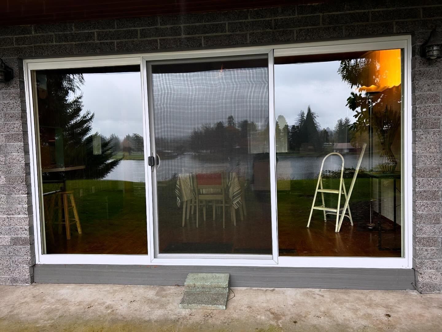 Sliding glass door reflects a pond, lawn, and chairs. A stepladder leans beside the door on a patio.