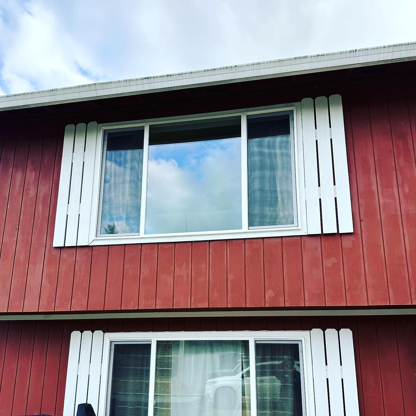 Red building with white-framed windows, and white vertical accents. Blue sky reflected in glass.