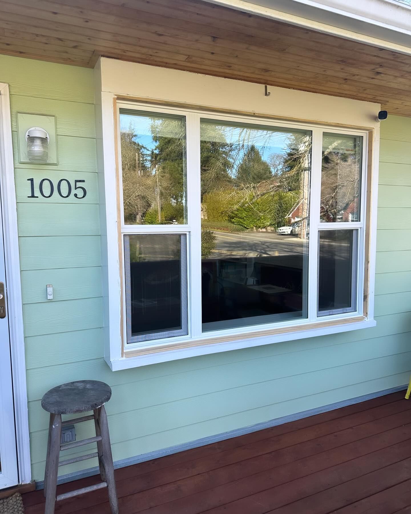 Exterior view of house with light green siding, white window trim, and a small wooden stool.