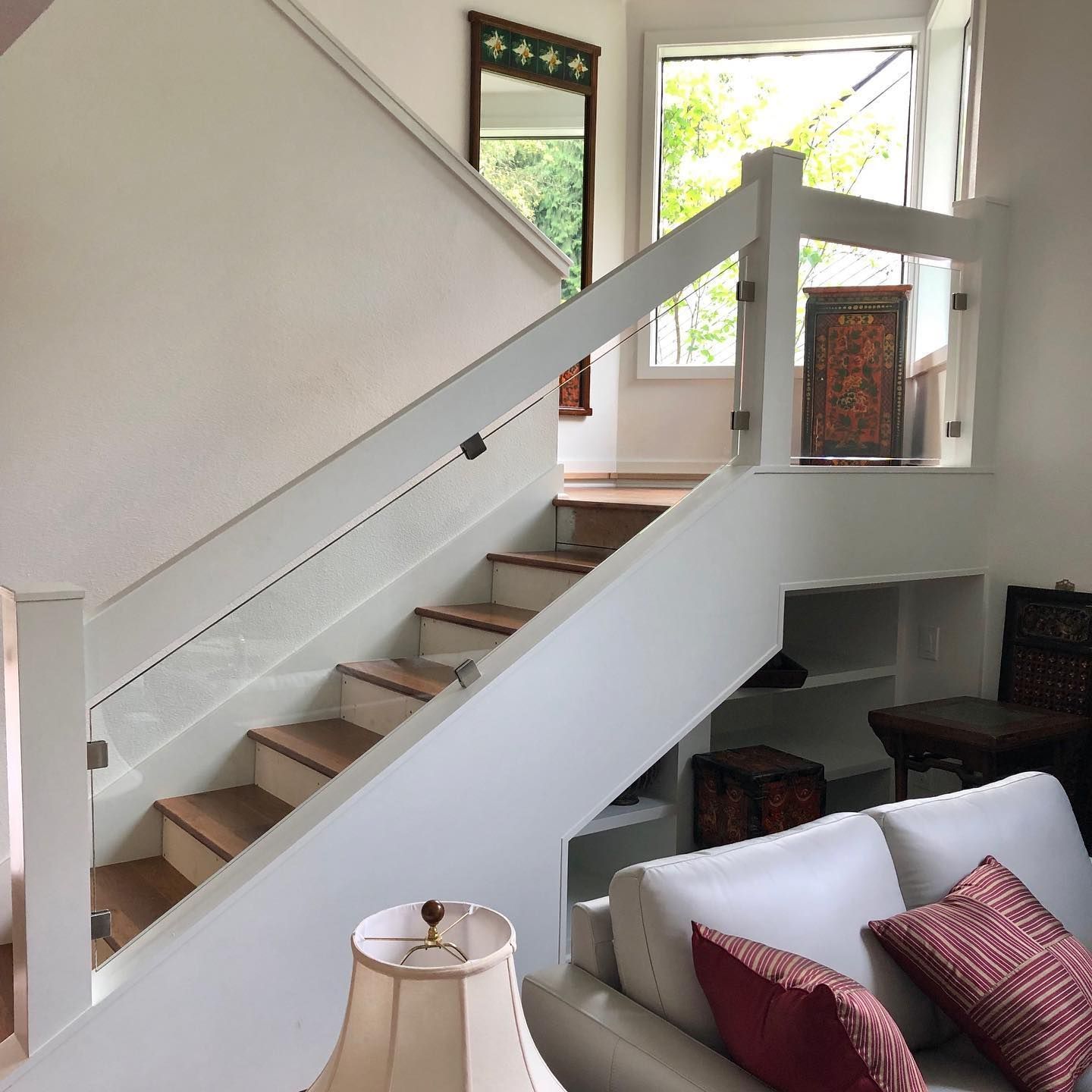 White staircase with glass railing, leading to a second floor. Wooden steps, white walls, and a window are visible.