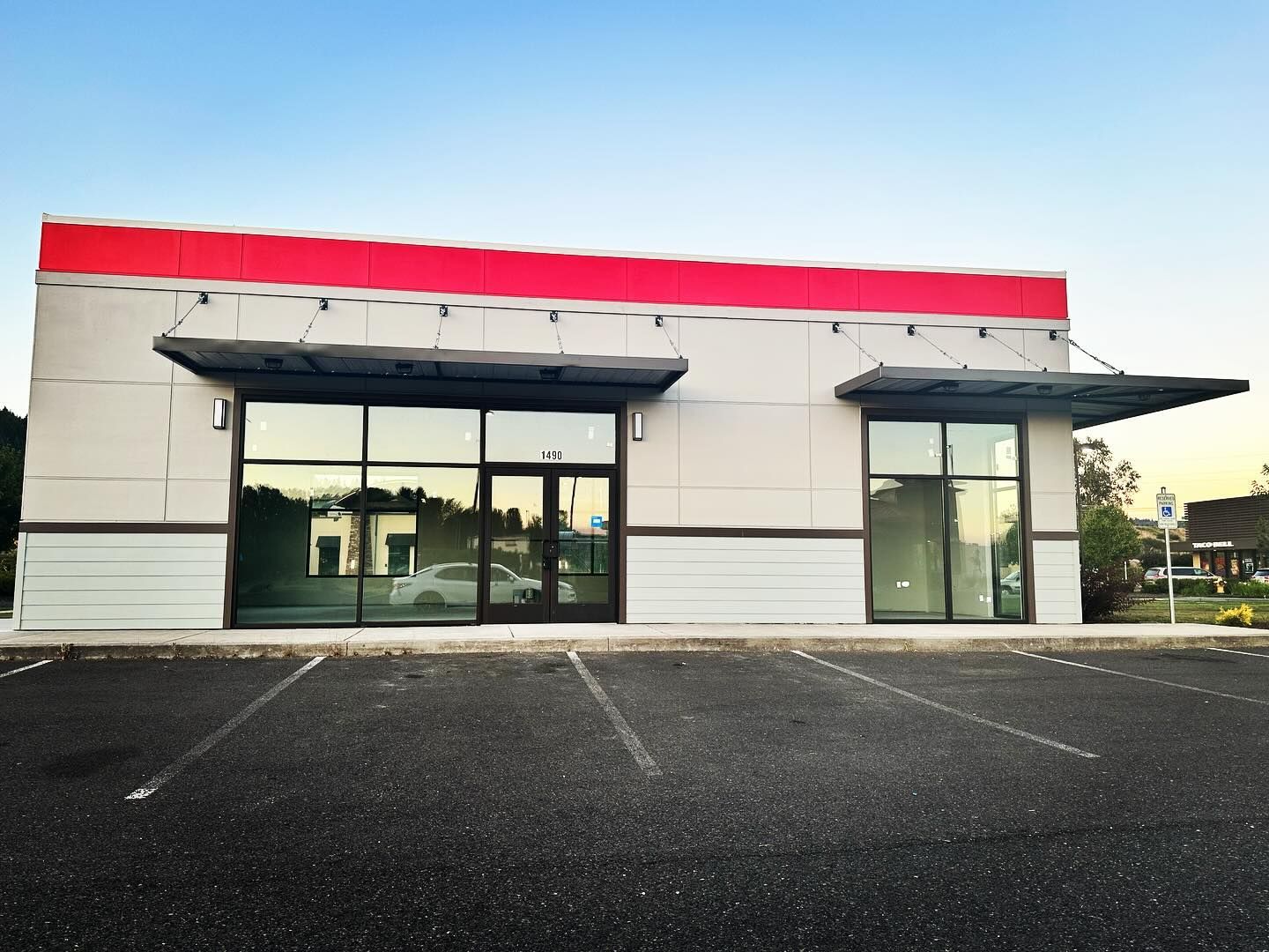 Exterior of a modern commercial building, empty, with large windows, awnings, and a red-topped facade.
