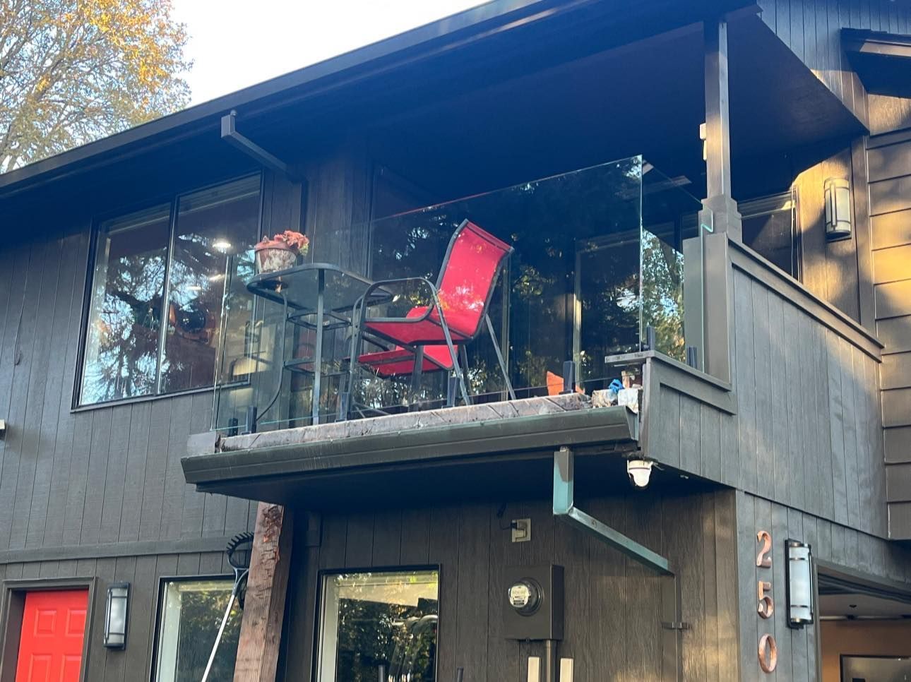 Black house with a balcony. Red chairs and table on balcony with glass railing.