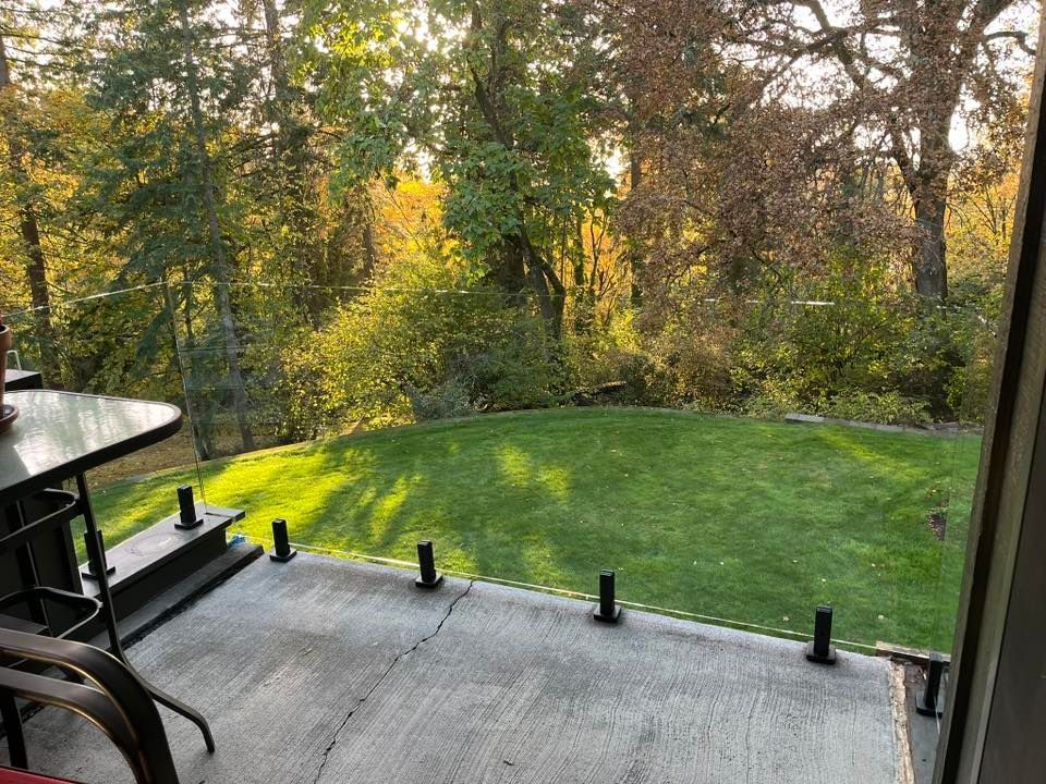 Patio overlooking a green lawn and trees with golden sunlight. Black railing posts along concrete.