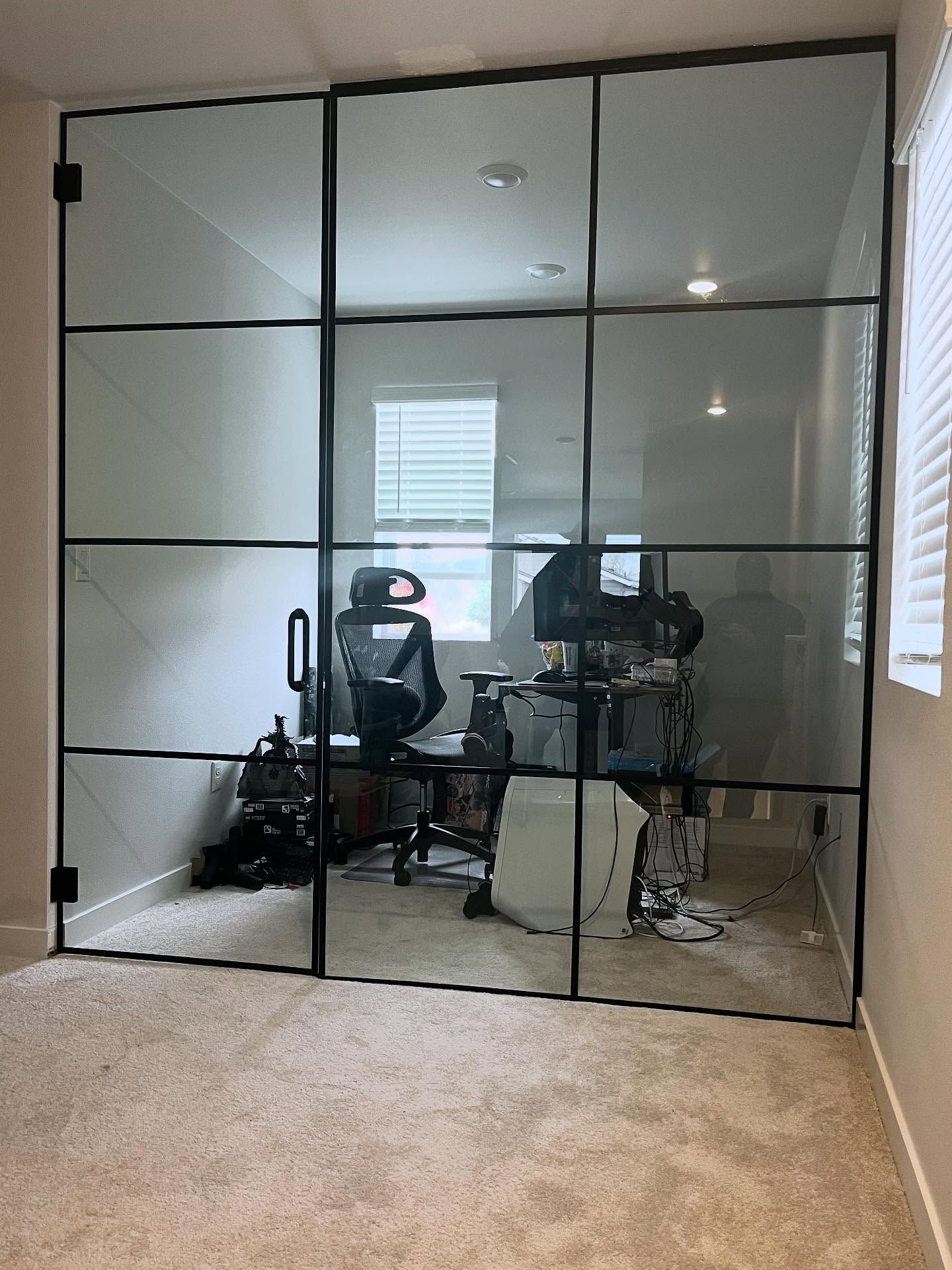 Glass-paneled office door with black frame, showing a desk with computer equipment inside the room.