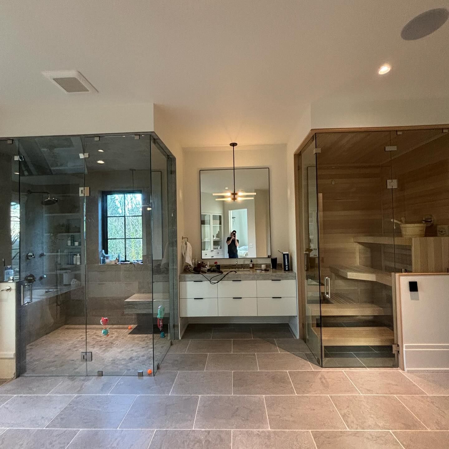 Modern bathroom with glass shower, sauna, and vanity on stone floor.