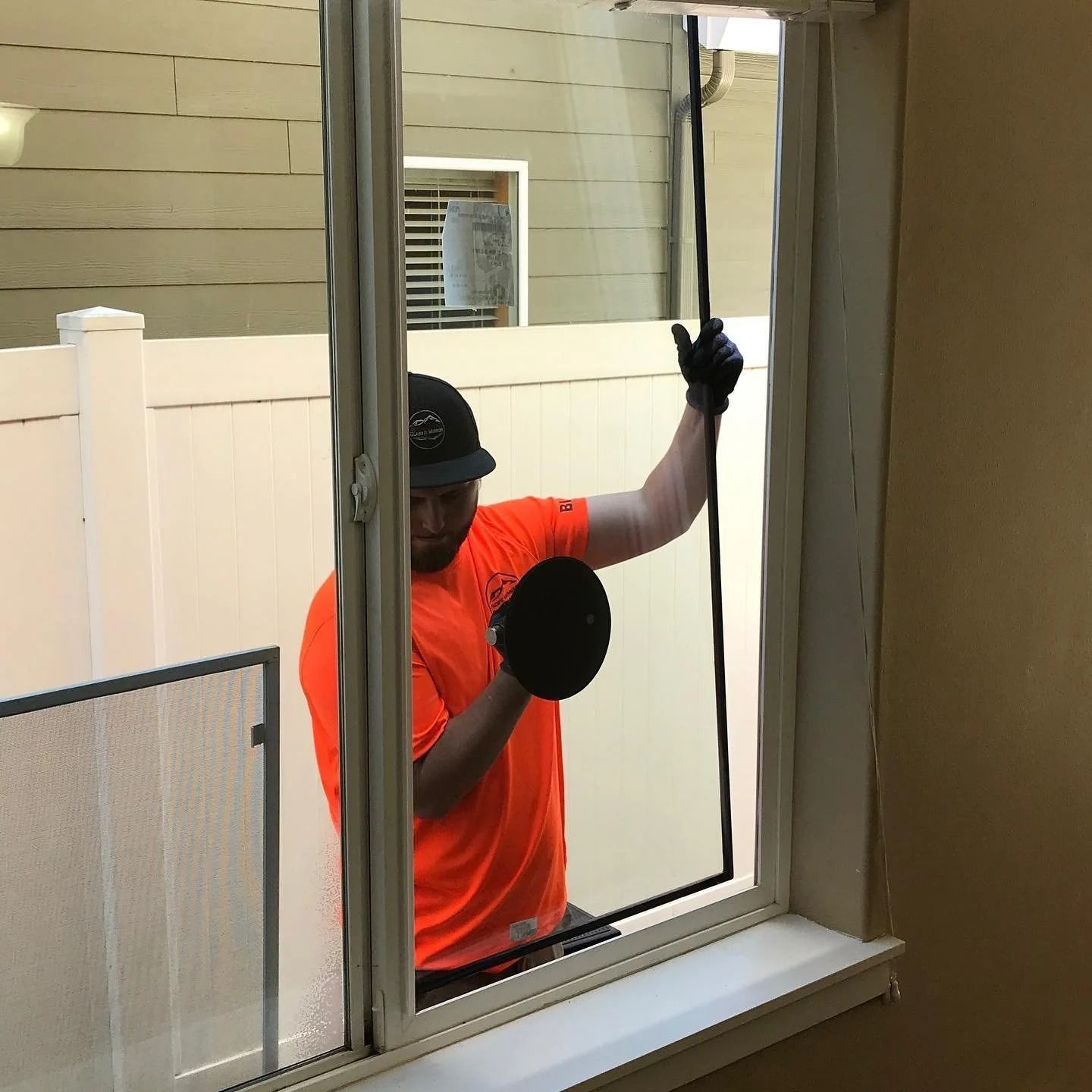 Person in orange shirt installing a window screen. Indoors, window, holding screen with black edging.