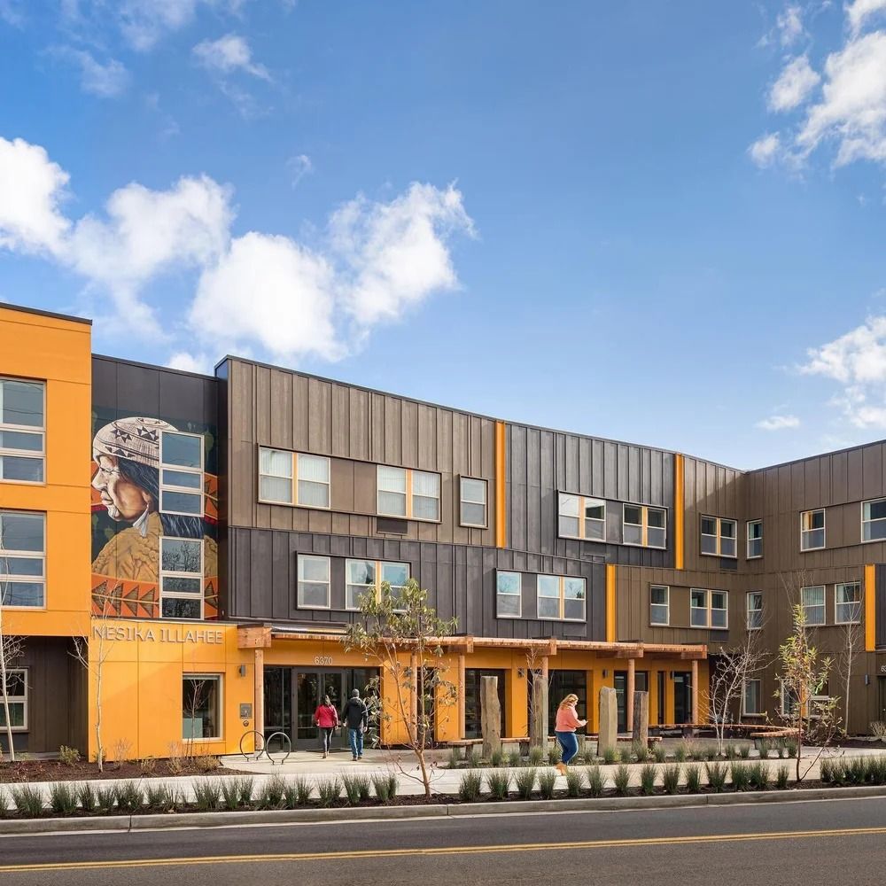 Exterior view of a modern multi-story building with a mural and people walking towards an entrance.