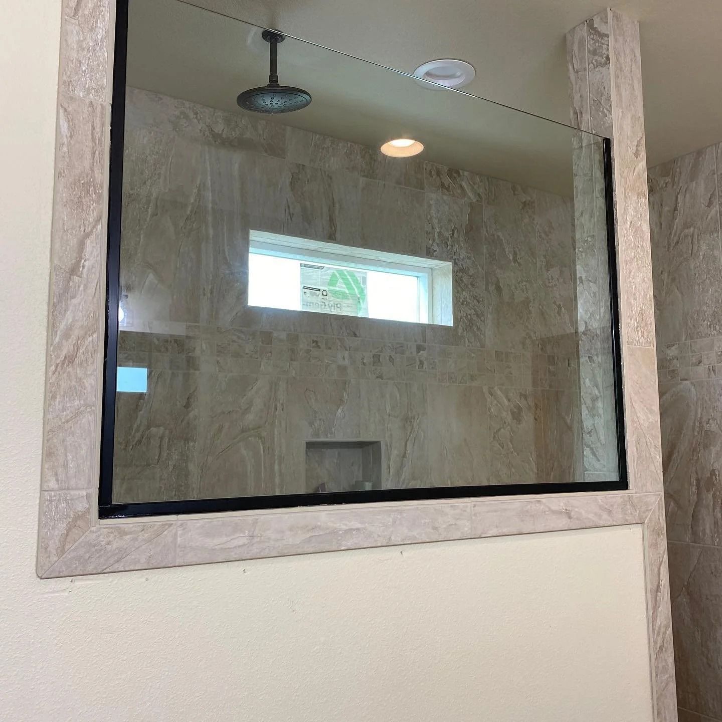 Glass shower enclosure with black trim, beige tile walls.