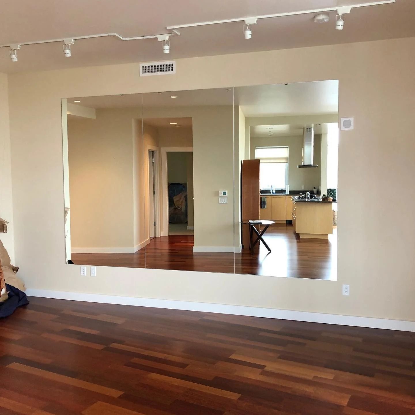 Large mirror reflecting a hardwood floor and interior rooms; a kitchen is visible in the distance.