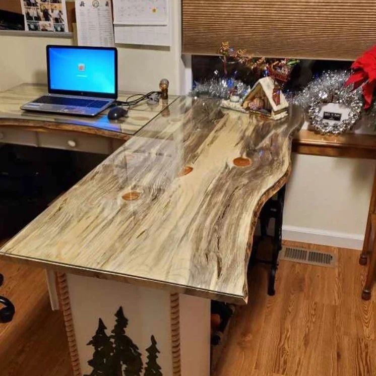 A wooden desk with a laptop, mouse, and Christmas decorations sits in a room with hardwood floors.