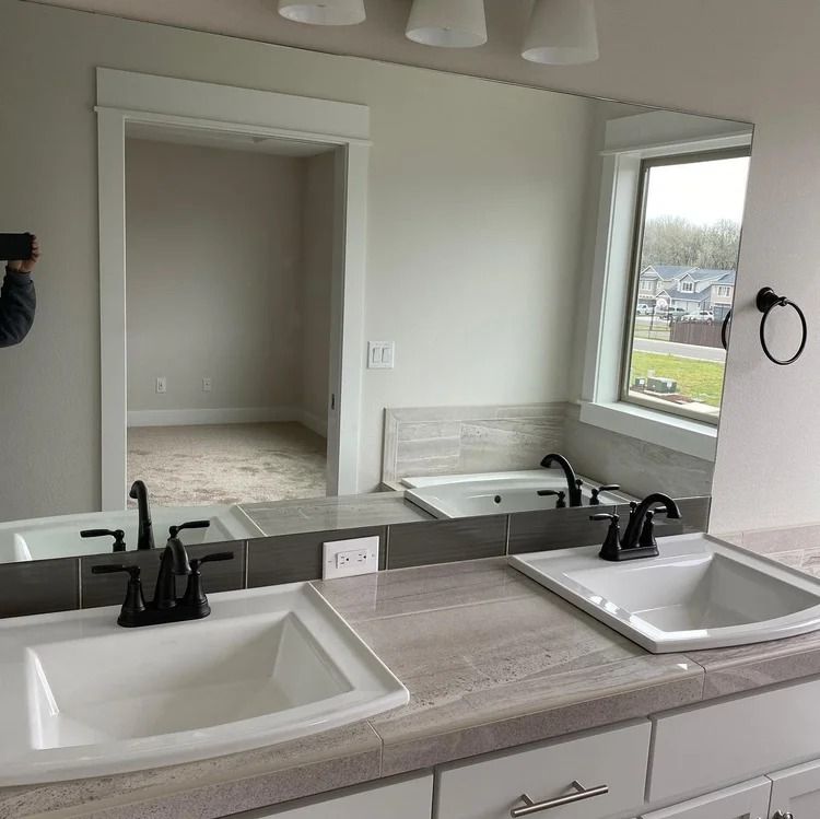 Bathroom with dual sinks, large mirror, and a view through a window. Black faucets and towel ring.