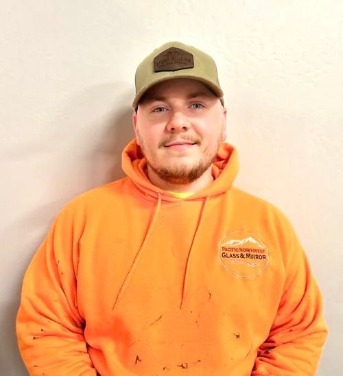 Man in orange hoodie and green cap smiles in front of a light wall.