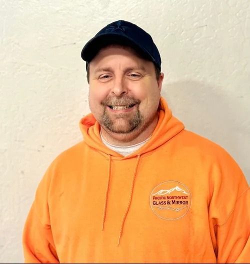 Man wearing orange sweatshirt and navy cap, smiling. Pacific Northwest Glass & Mirror logo visible.