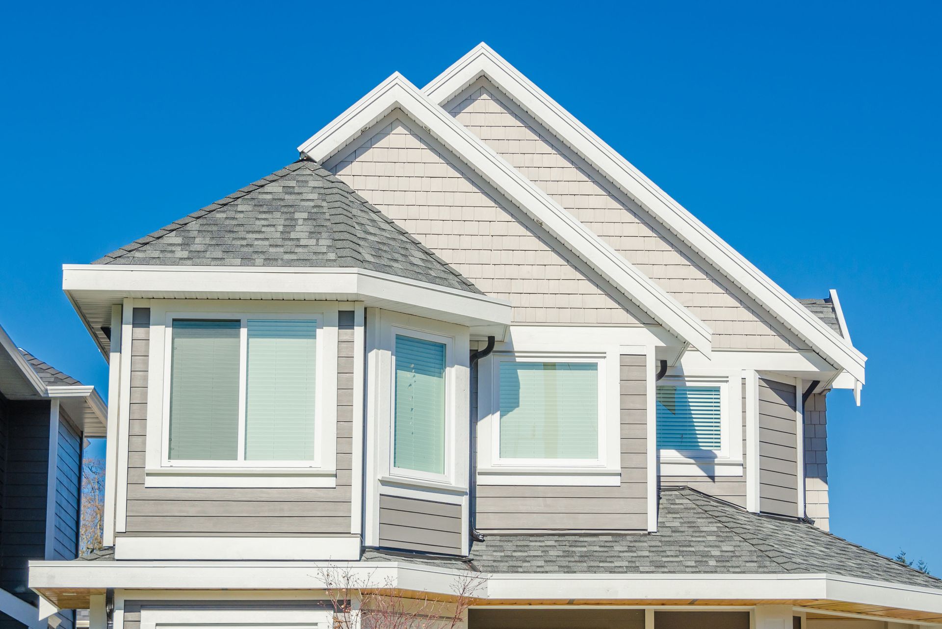 Two-story house with light siding, gray shingles, and white trim under a blue sky