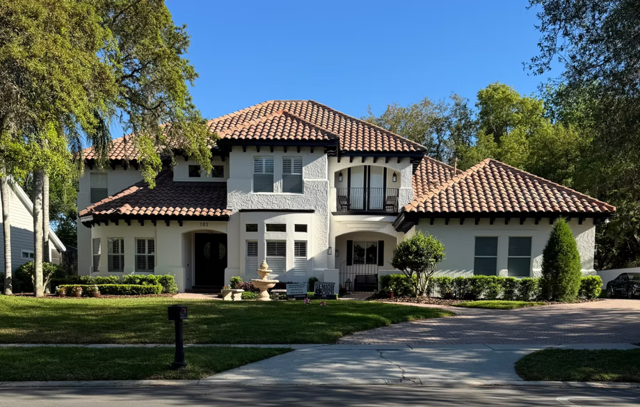 Large white Mediterranean-style house with a red tile roof and front lawn under clear blue skies