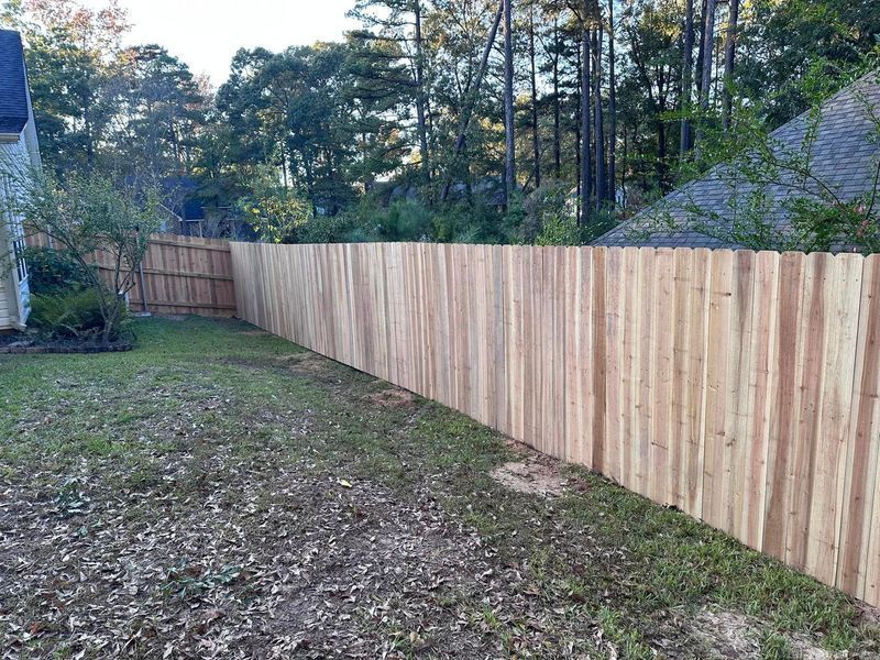 Wooden fence in a backyard, enclosing the space. Green grass and trees are visible.