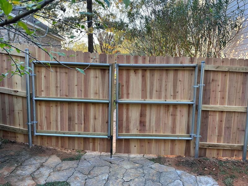 Wooden fence with two matching gates, gray metal frames, set in a backyard.