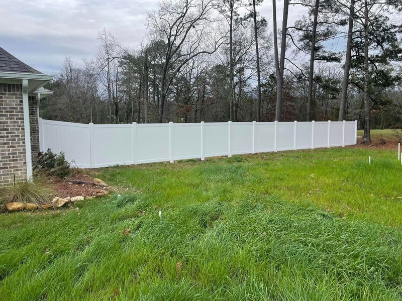 White vinyl fence bordering a grassy yard with trees in the background.