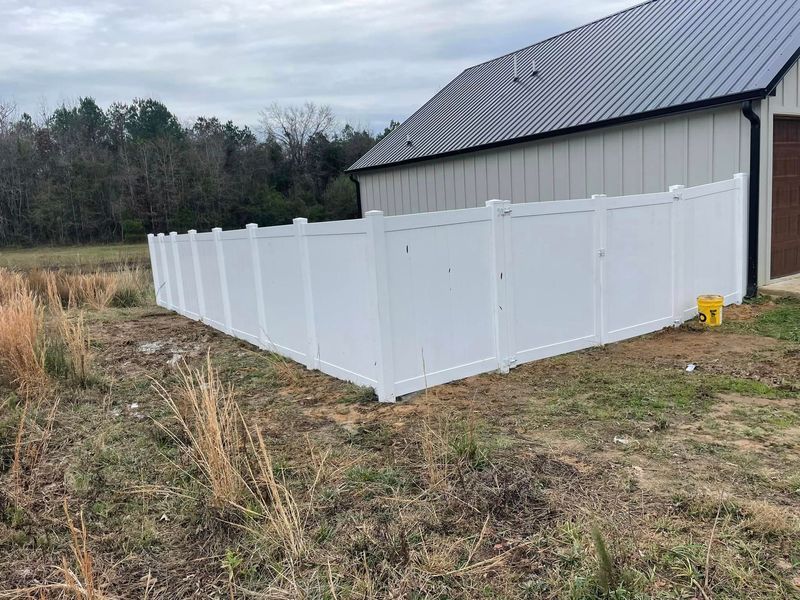 White vinyl fence around a building with a dark roof, on a grassy lot under cloudy skies.