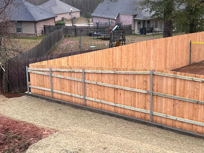 Wooden fence in a backyard, brown with gray supports, separating a lawn from other houses.