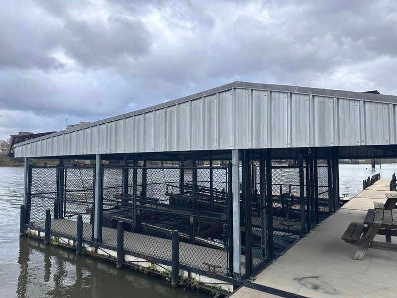 Boat dock shelter with metal roof on a cloudy day. The shelter has mesh sides and is on a concrete pier.