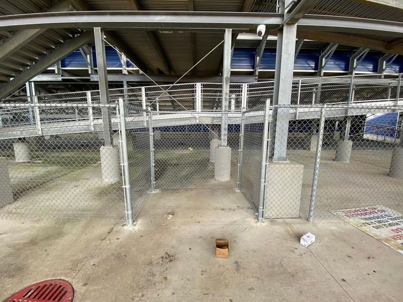 Chain link fence gate under stadium seating. Gray concrete floor, supports, and some trash.