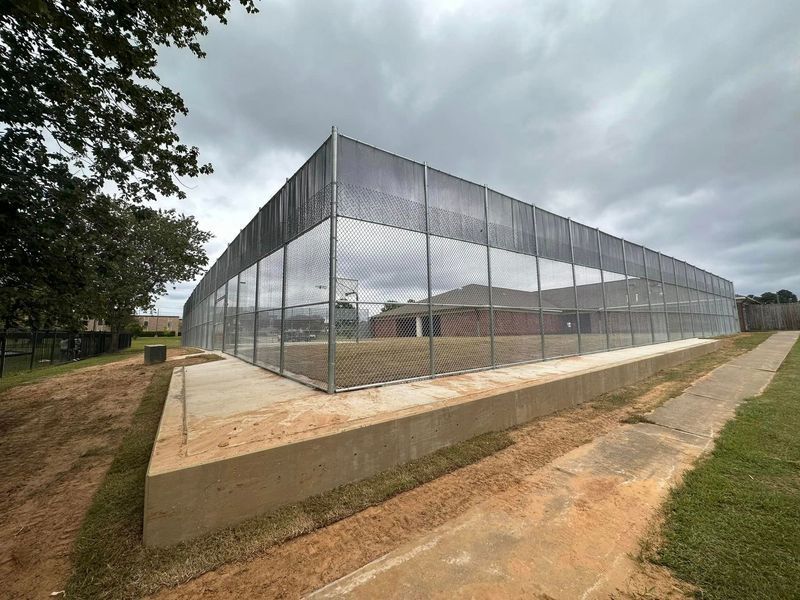 A large, fenced enclosure on a concrete foundation, likely for security. Gray overcast sky.
