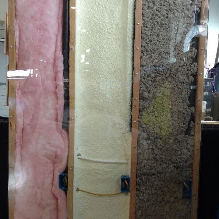 Three wall insulation types displayed in clear-sided sections: pink fiberglass, white spray foam, and gray cellulose.