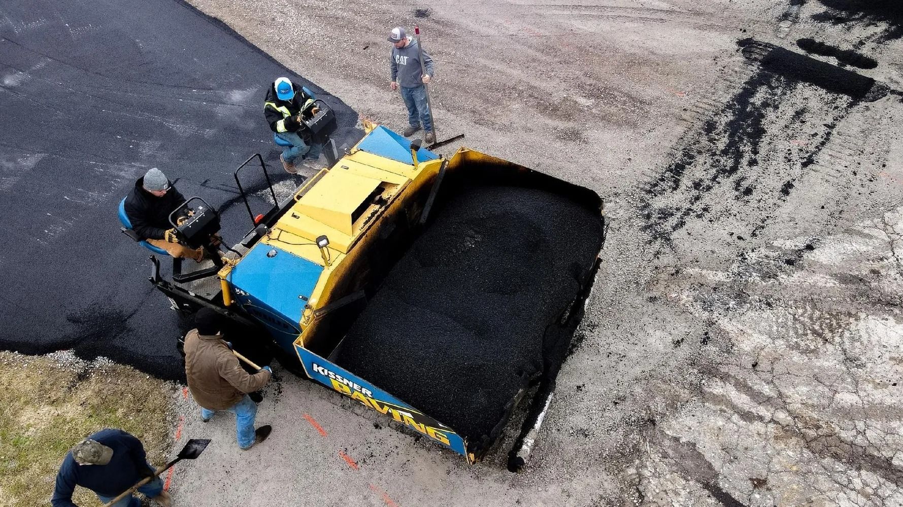 Asphalt paver with workers; laying new road surface. Black asphalt, blue and yellow machine, outdoors.