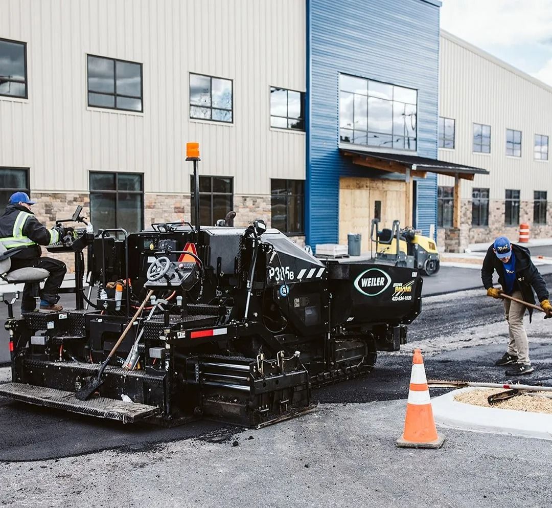 Asphalt paving machine laying fresh asphalt on a road, with workers guiding and shoveling the material.